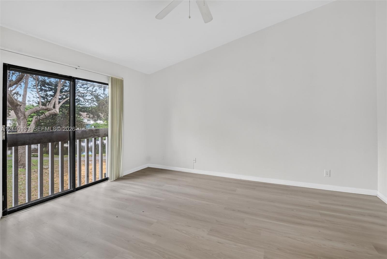 Interior space featuring vaulted ceilings, wood-finish flooring, a ceiling fan, and sliding glass doors with access to an exterior balcony