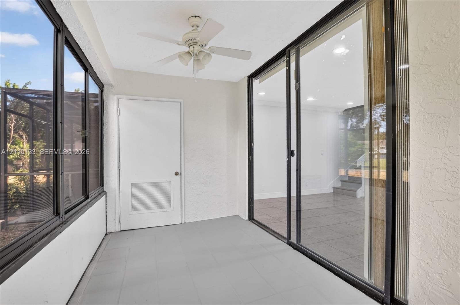 Enclosed porch featuring tile flooring, metal-framed screen wall panels, integrated ceiling fan, and sliding glass panel doors