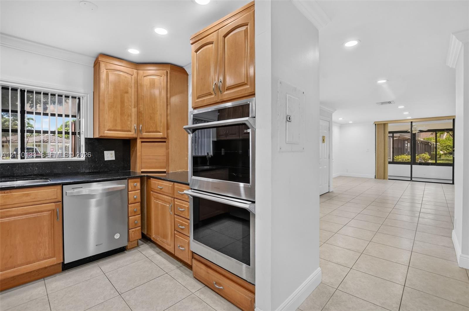 Kitchen featuring wood cabinetry, dark stone countertops, stainless steel double wall ovens, stainless steel dishwasher, and tile flooring