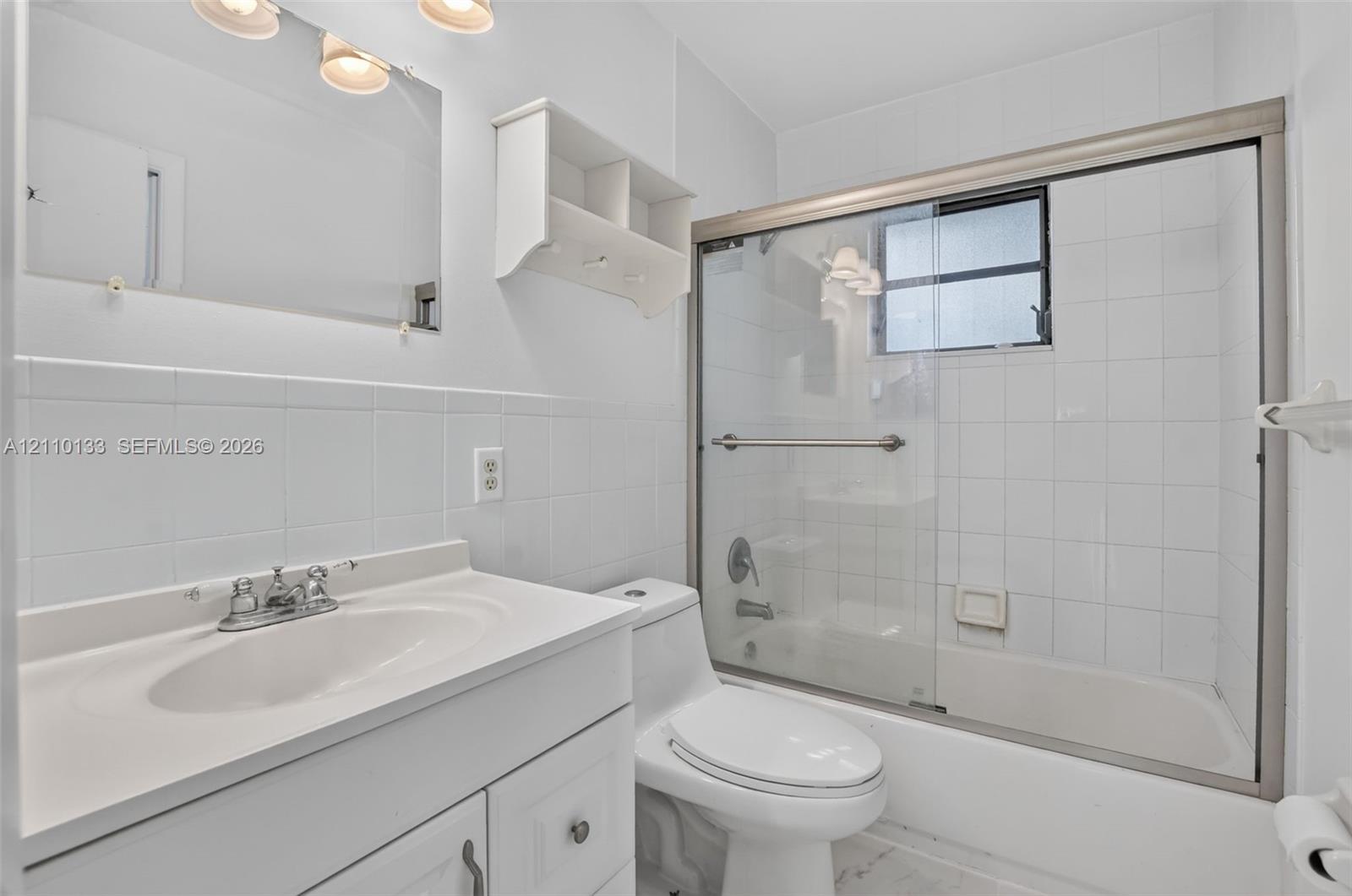 Bathroom featuring a white vanity with an integrated countertop sink, wall-mounted cabinetry, a full-width mirror, and a tub-shower combination with sliding glass doors