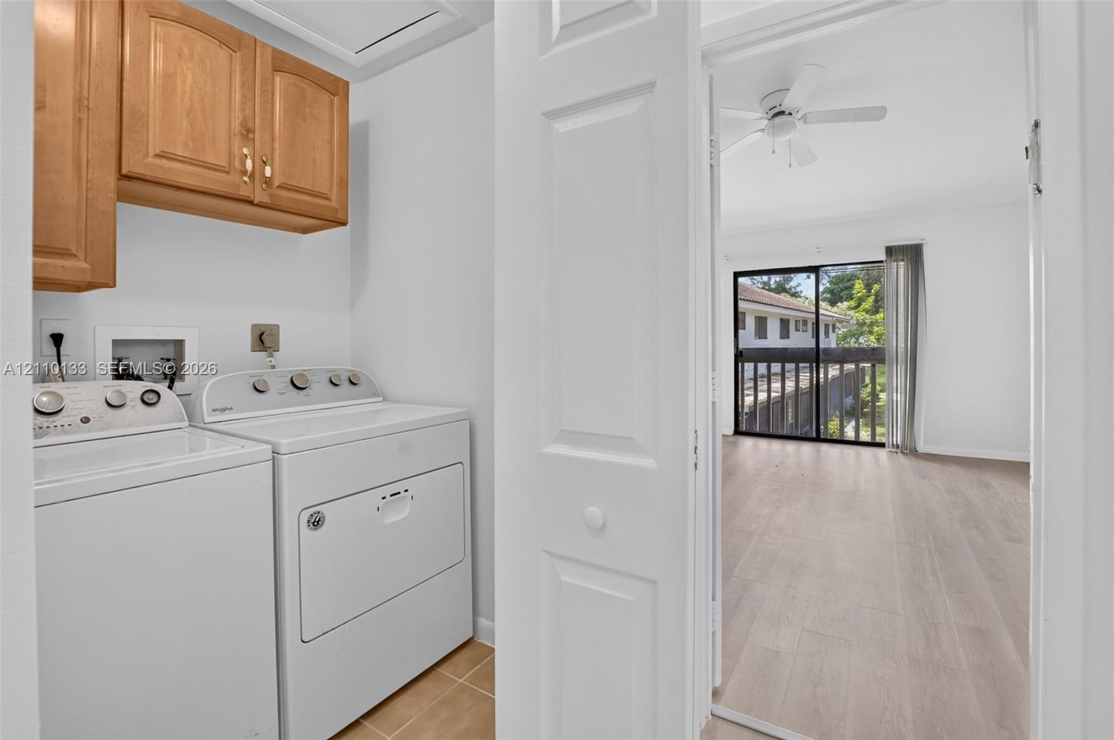 Laundry area featuring upper wood-finish cabinetry, tile flooring, and white washer and dryer units