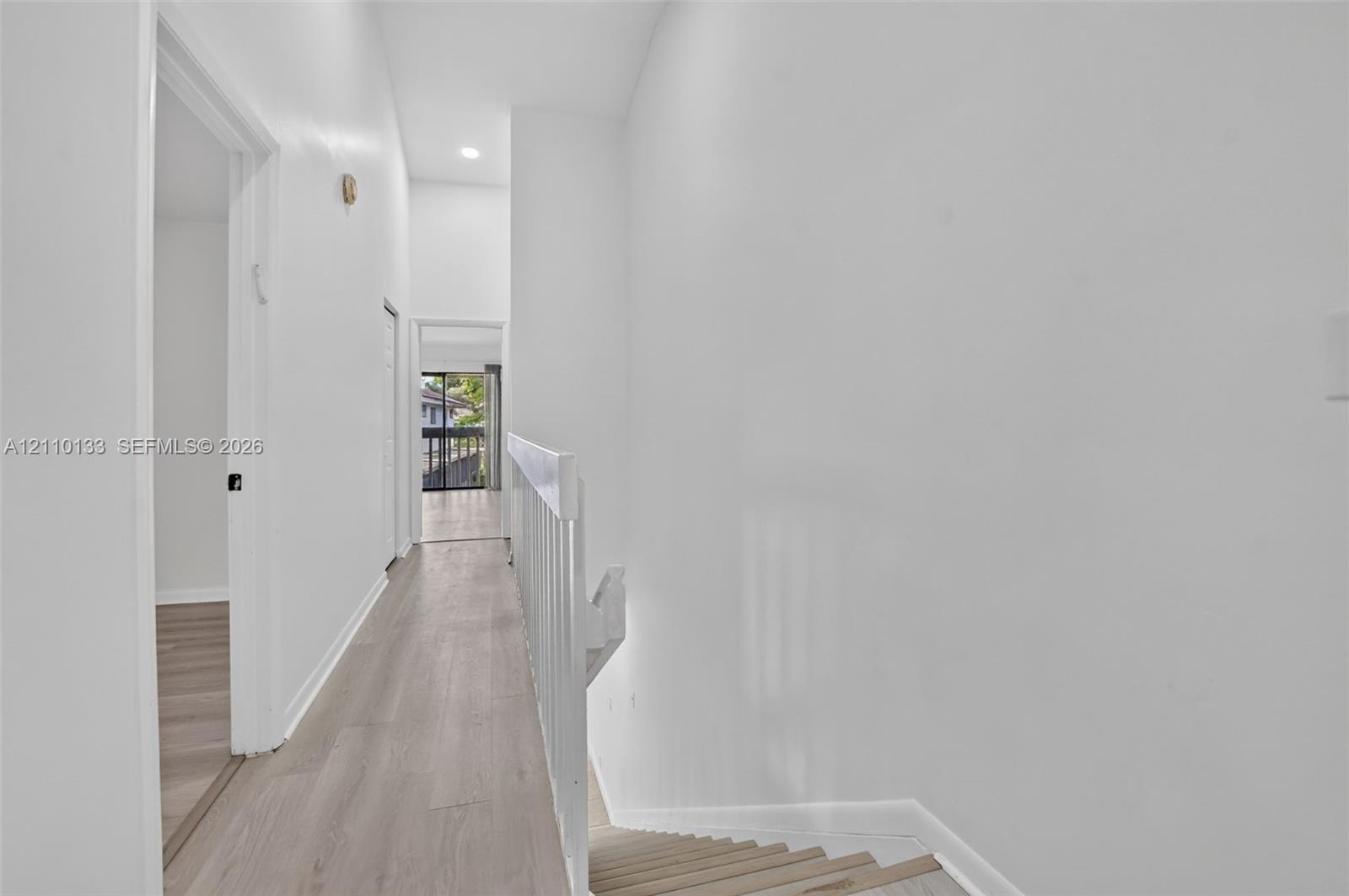 Hallway featuring wood-finish flooring, vaulted ceilings, recessed lighting, and a white balustrade railing