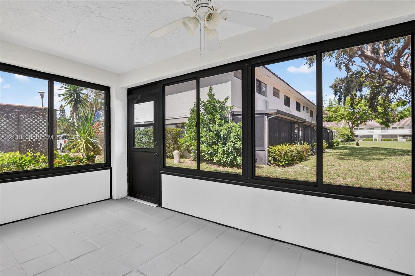 Enclosed sunroom featuring large-pane windows, a dark-framed entry door, tile flooring, and a ceiling-mounted light fixture