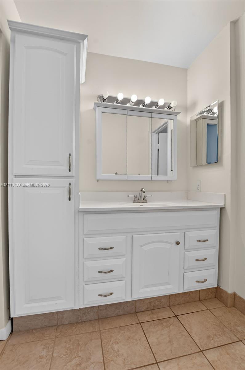 White cabinetry vanity featuring integrated tall storage, solid-surface countertop with an undermount sink, multi-bulb overhead lighting, and triple-panel mirrored medicine cabinet