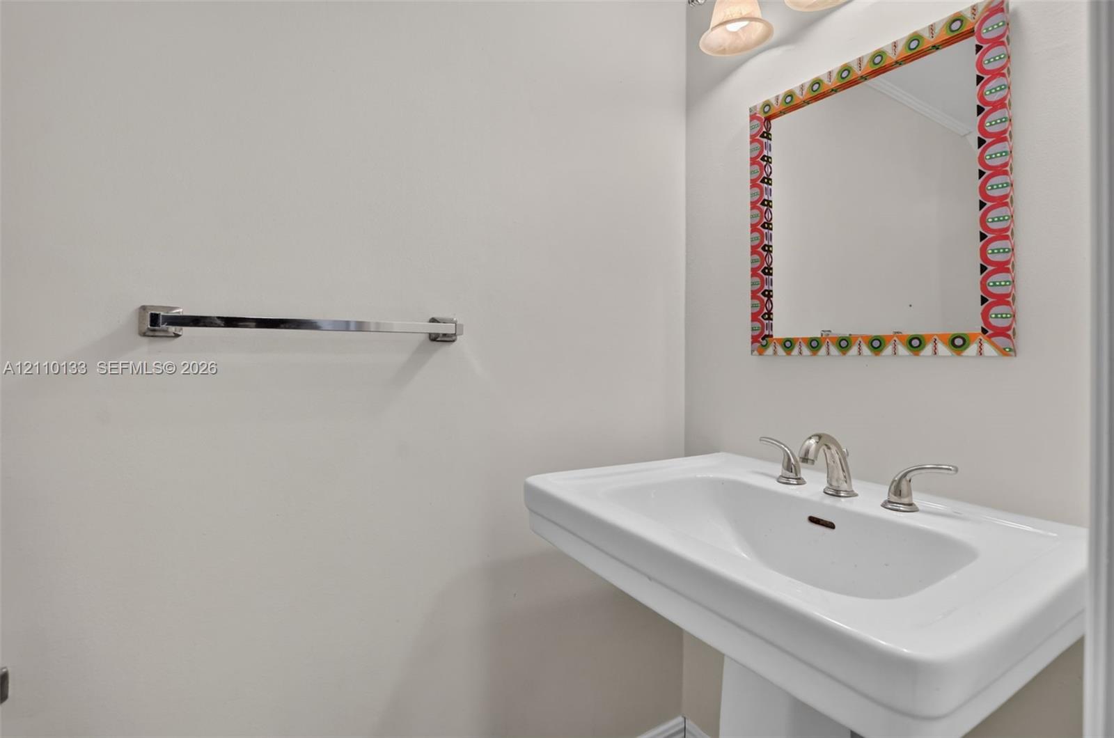 Wall-mounted pedestal sink featuring a widespread polished chrome faucet, polished chrome towel bar, and multi-light vanity fixture