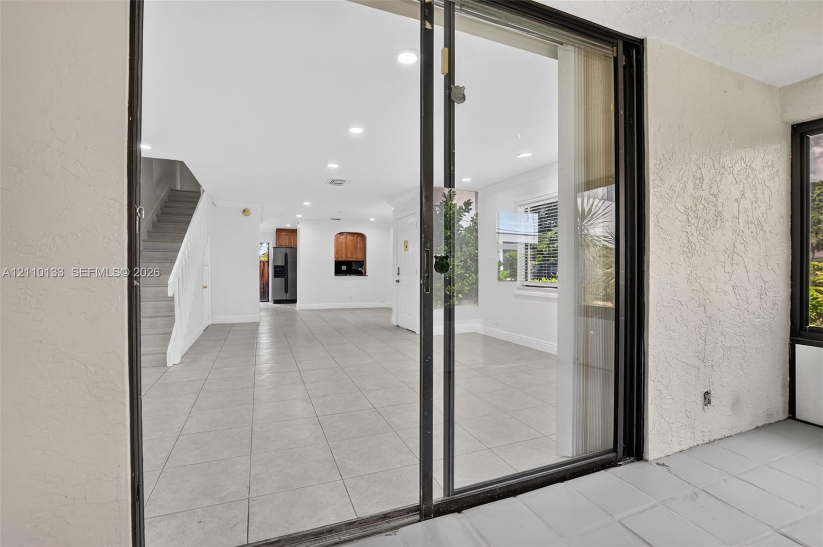 Sliding glass doors with black frames, neutral tile flooring, recessed lighting, and a built-in arched wall opening