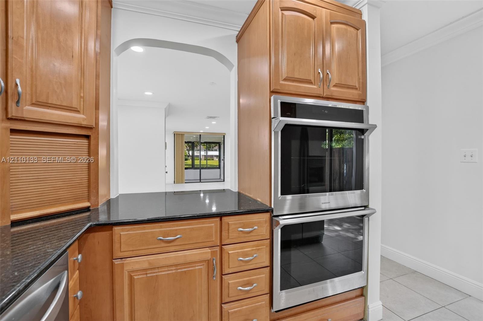 Kitchen featuring wood cabinetry, integrated double wall ovens, dark stone countertops, and crown molding