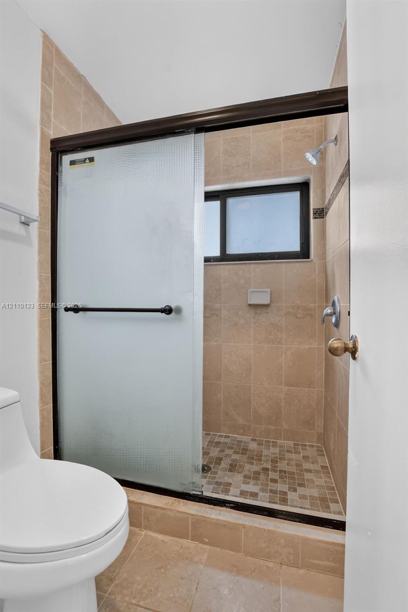 Walk-in shower featuring glass sliding doors with a dark frame, beige wall tile, stone mosaic floor tile, and a built-in recessed soap niche