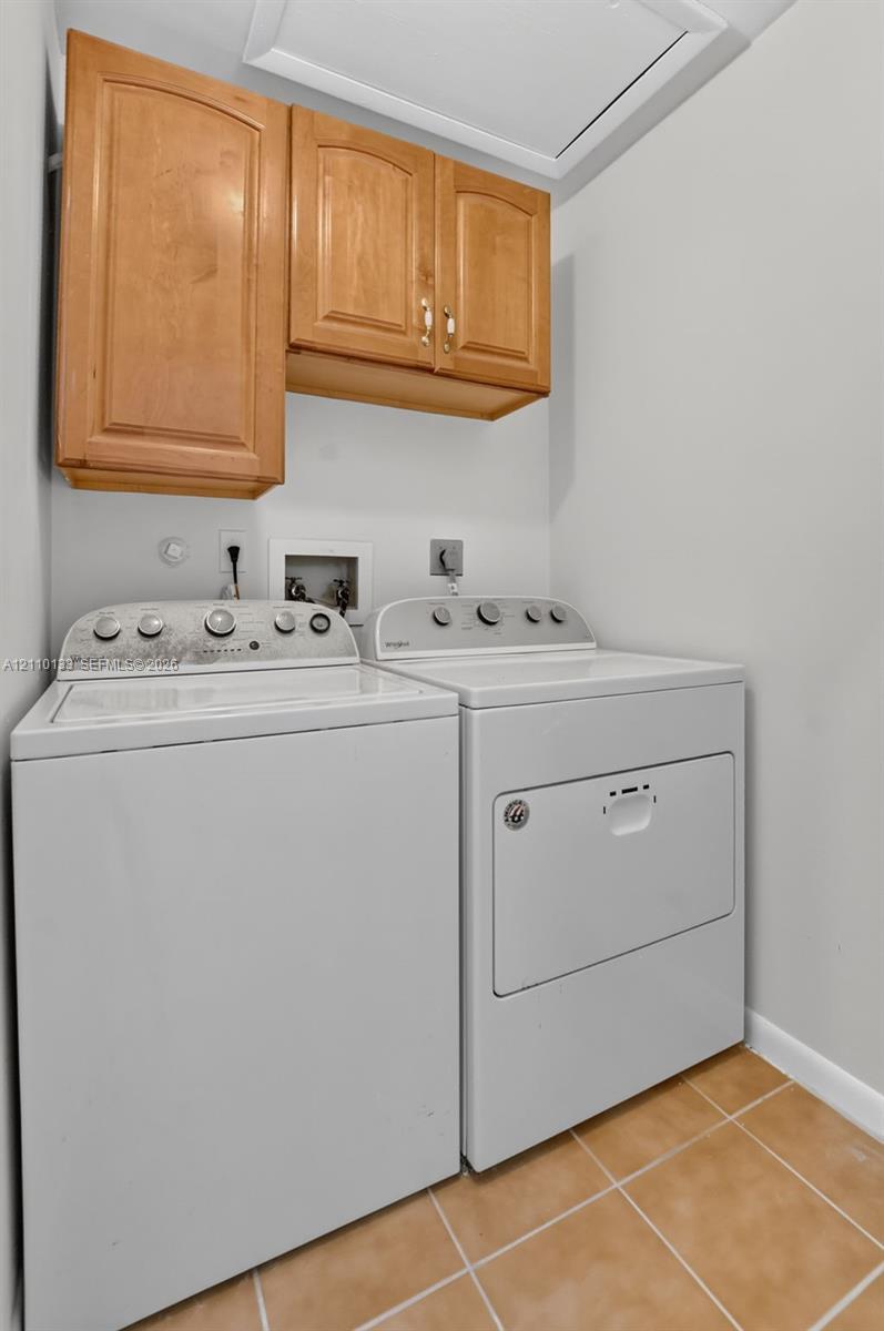 Laundry area featuring wood-finish wall-mounted cabinetry, ceramic tile flooring, and dedicated washer and dryer hookups