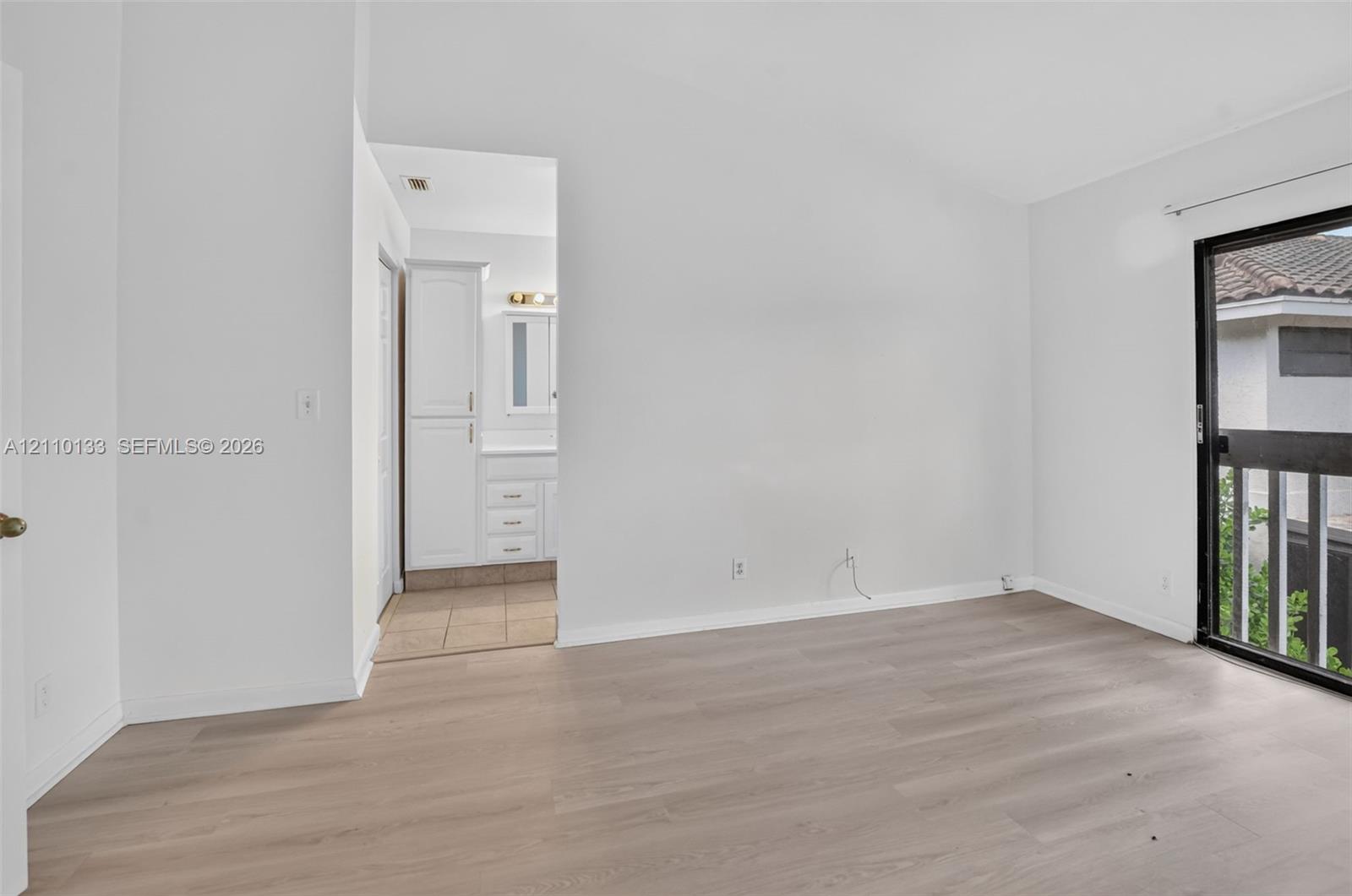 Neutral-toned room with wood-finish flooring, featuring a glass sliding door and direct sightline to a white cabinetry vanity unit