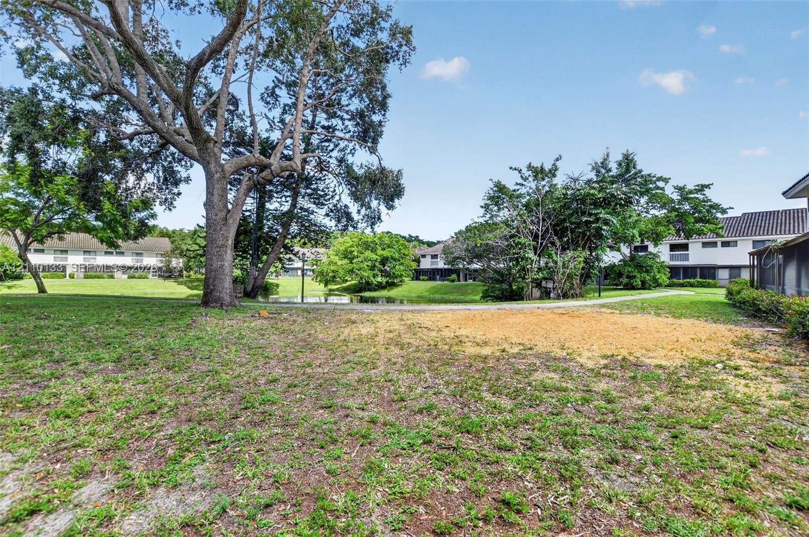 Expansive green space featuring mature trees, a concrete pathway, and a central pond