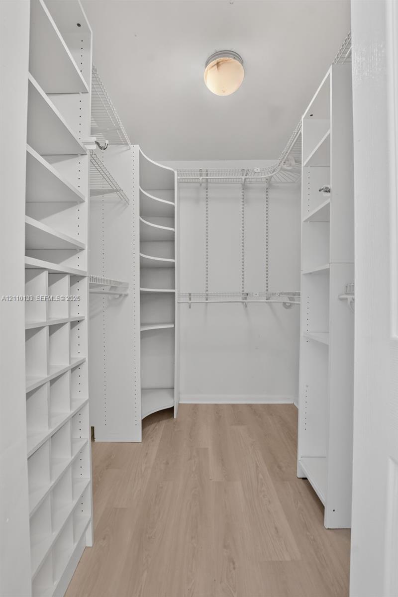 Walk-in closet featuring white built-in shelving, curved corner units, wire hanging racks, and wood-finish flooring