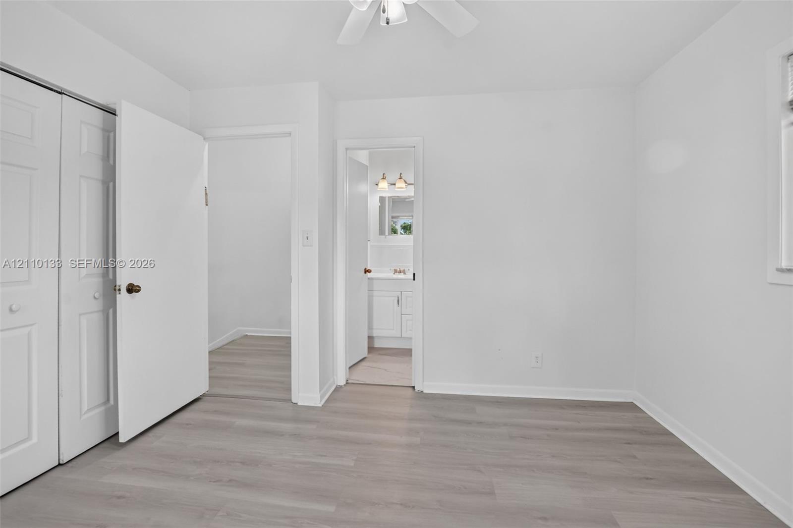 Room featuring wood-finish flooring, white walls, a ceiling fan, and double-door closet cabinetry