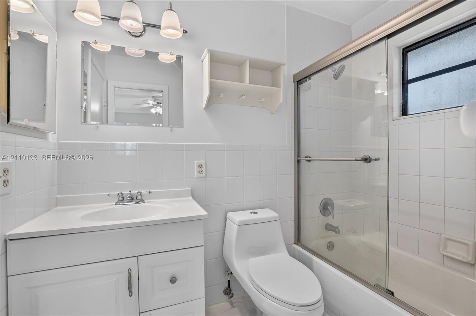 Bathroom featuring a white vanity cabinet, ceramic tile wall surround, sliding glass shower door enclosure, and built-in wall-mounted shelving