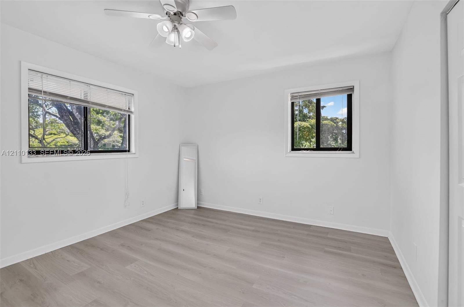 Neutral-toned interior featuring wood-finish flooring, dual windows with integrated blinds, and a ceiling-mounted light fixture with a central fan