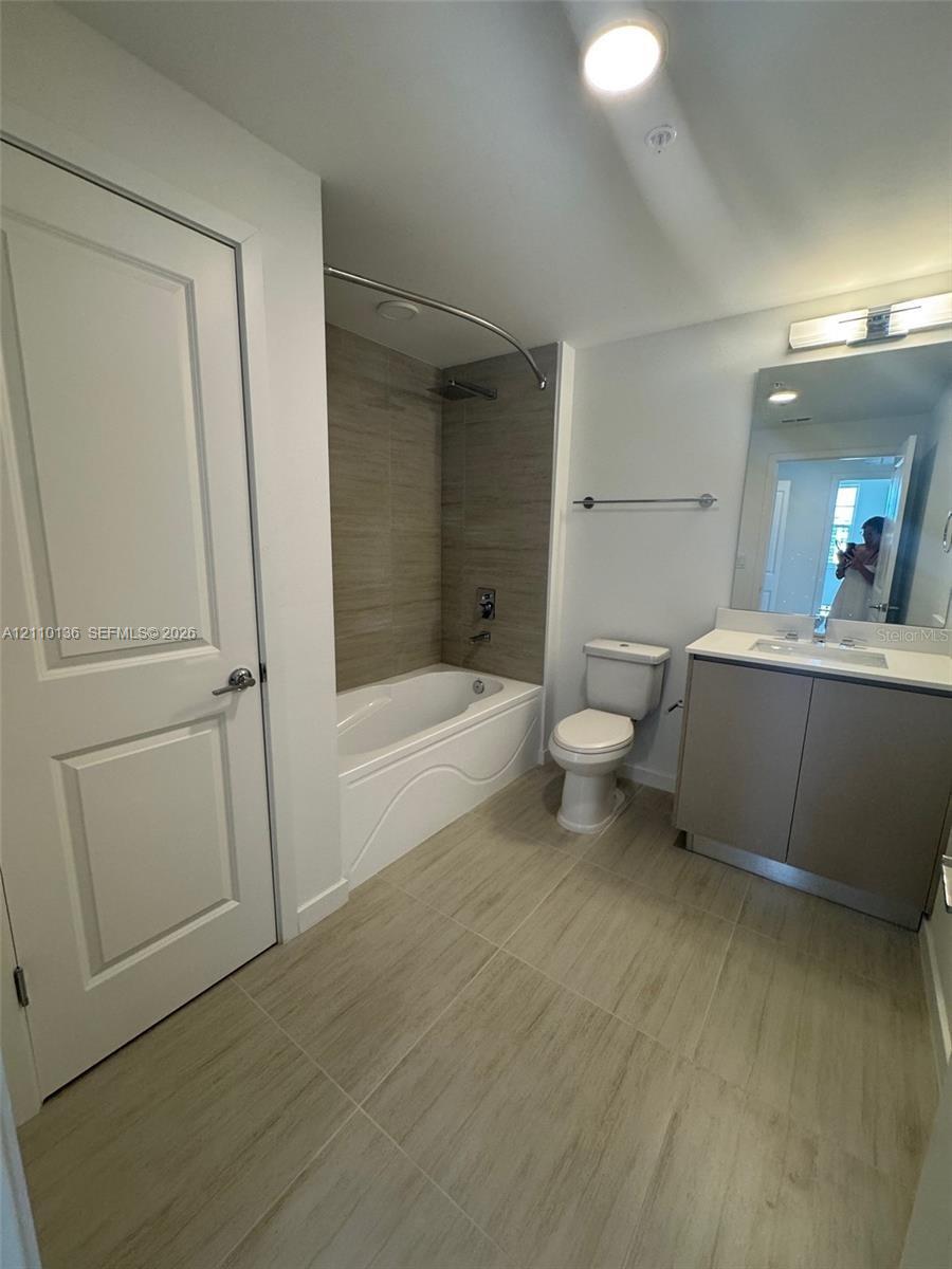 Bathroom featuring a vanity with a light-toned countertop, a shower-tub combination with full-height neutral wall tiling, and wood-finish tile flooring