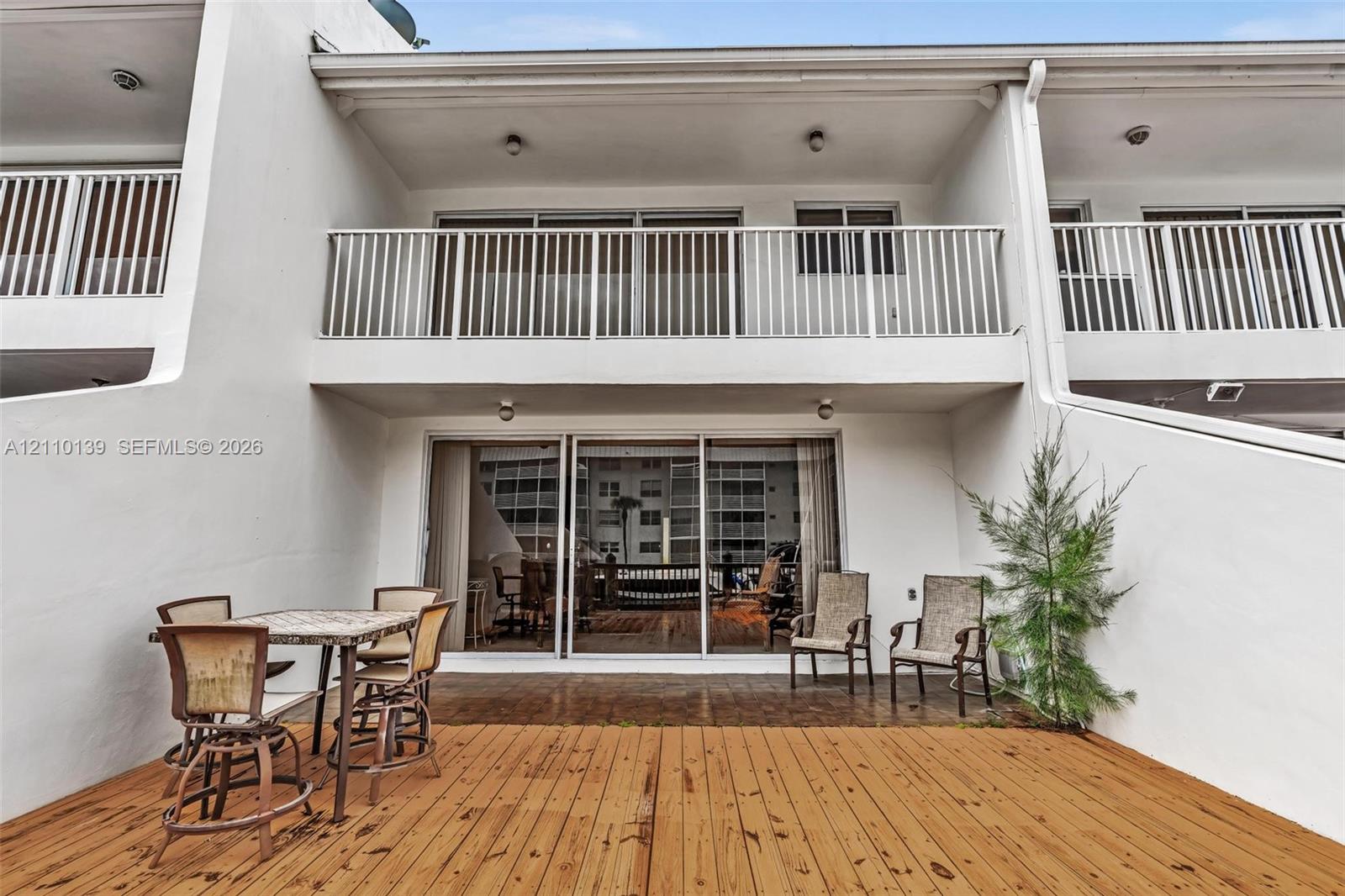 Exterior terrace featuring a wood-finish deck, sliding glass door entry, and second-story balcony with white metal railing