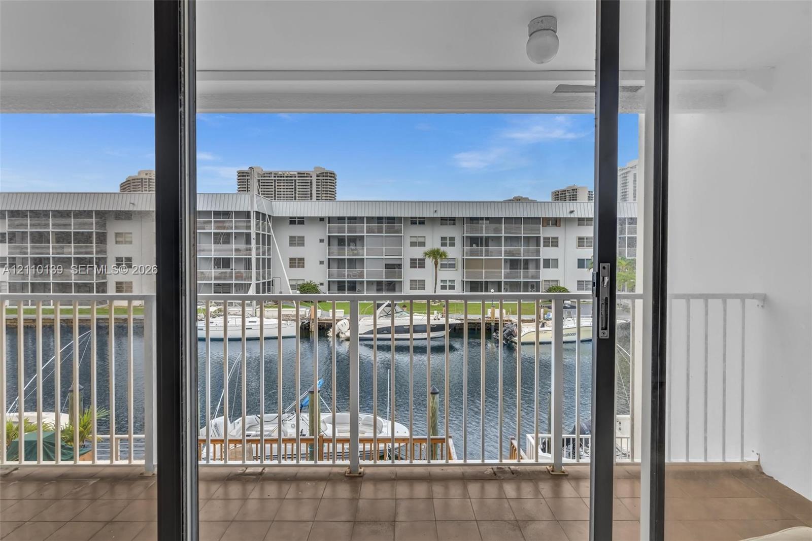 Covered balcony with neutral tile flooring, white metal railing, and sliding glass entry door