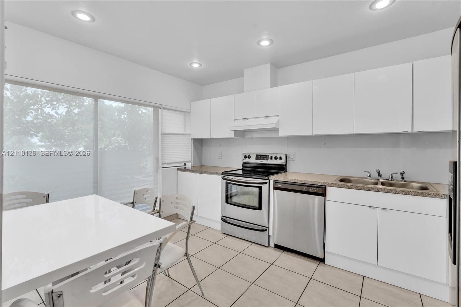 Kitchen featuring white flat-panel cabinetry, stainless steel appliances, neutral countertops, tile flooring, and recessed lighting