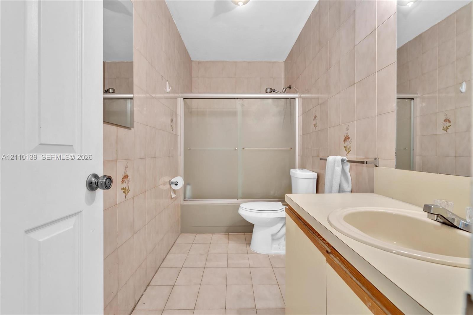 Bathroom featuring full-height wall tiling, a combination tub and shower enclosure with sliding glass doors, a vanity with a countertop-integrated basin, and large-format floor tiling