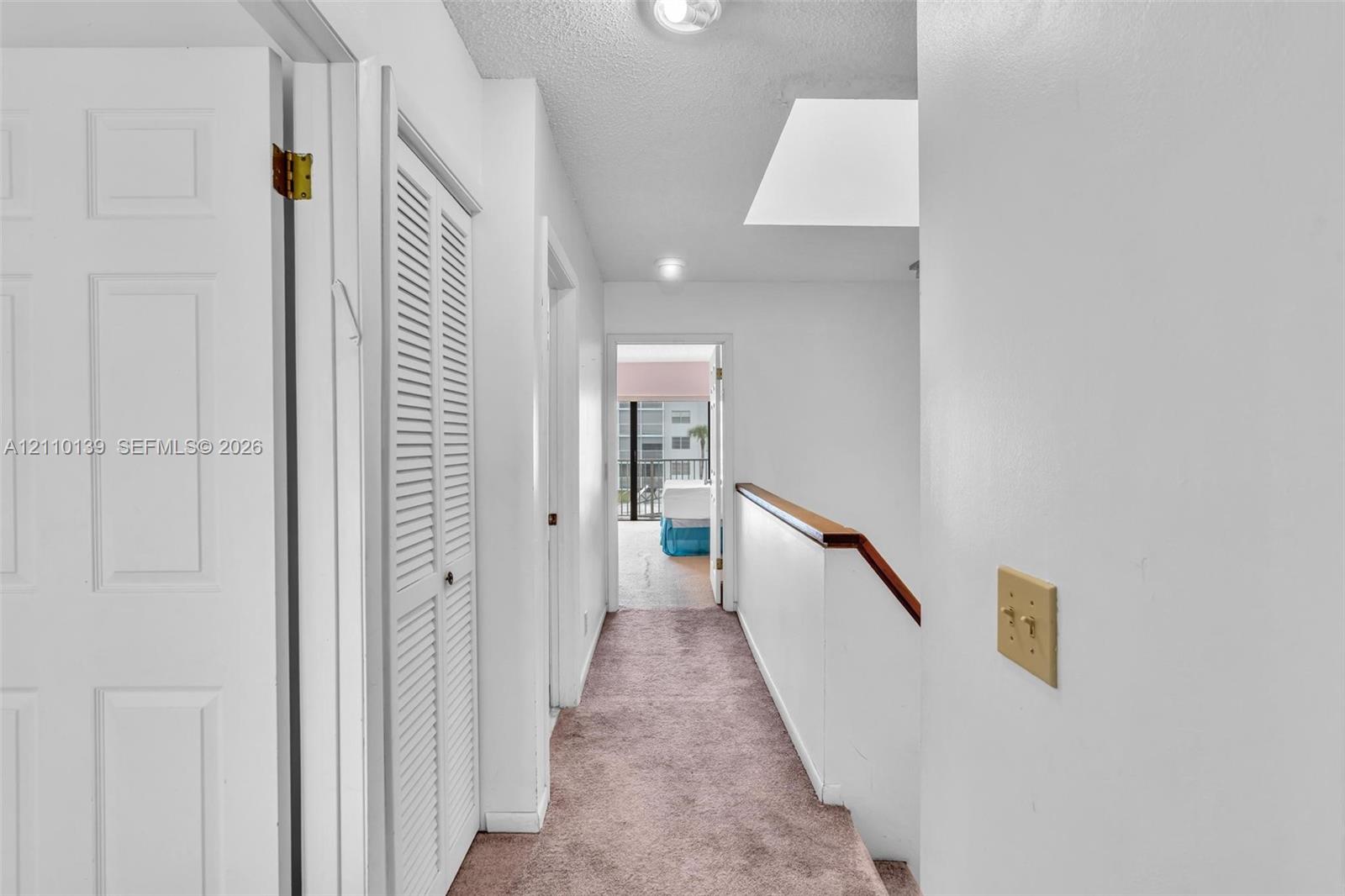 Interior hallway featuring carpeted flooring, a skylight, multi-panel doors, louvered-style closet doors, and a staircase with a wooden handrail