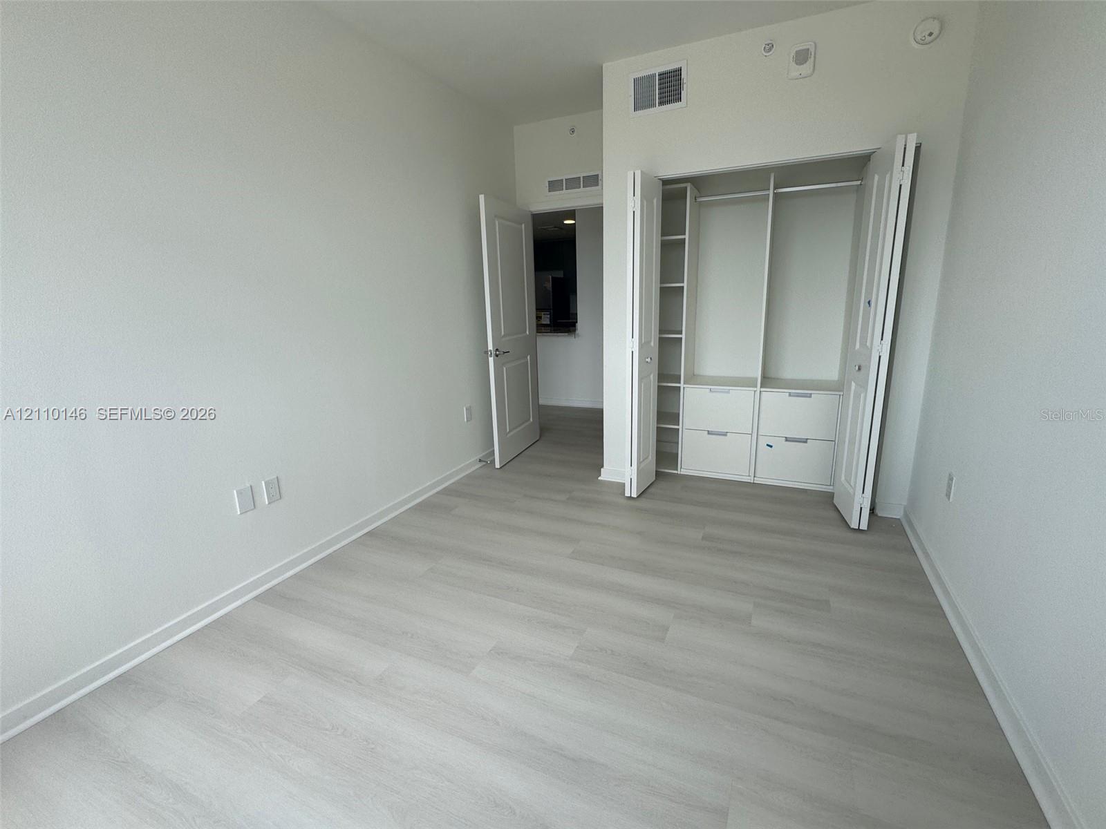 Wood-finish flooring, interior closet with custom built-in shelving and drawers, and paneled swinging door Wood-finish flooring, interior closet with custom built-in shelving and drawers, and paneled swinging door