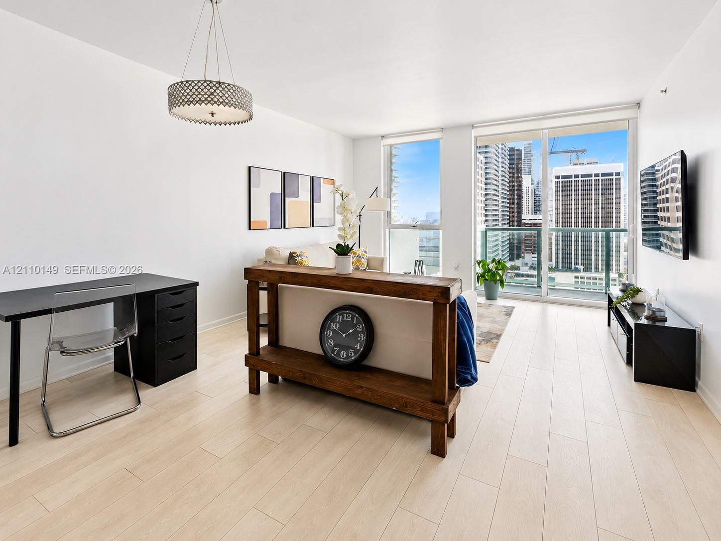 Light-toned wood-finish flooring, floor-to-ceiling windows, glass-panel balcony door, and a circular drum pendant light fixture Light-toned wood-finish flooring, floor-to-ceiling windows, glass-panel balcony door, and a circular drum pendant light fixture