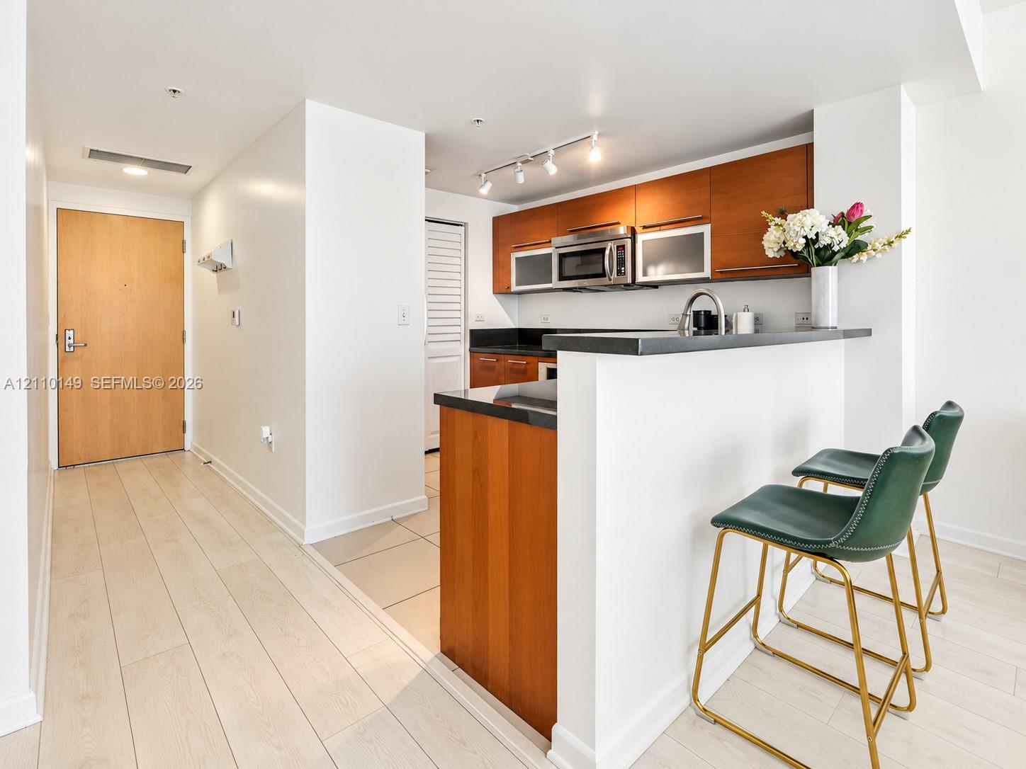 Kitchen featuring wood-finish cabinetry, dark stone countertops, stainless steel appliances, and a breakfast bar with track lighting Kitchen featuring wood-finish cabinetry, dark stone countertops, stainless steel appliances, and a breakfast bar with track lighting