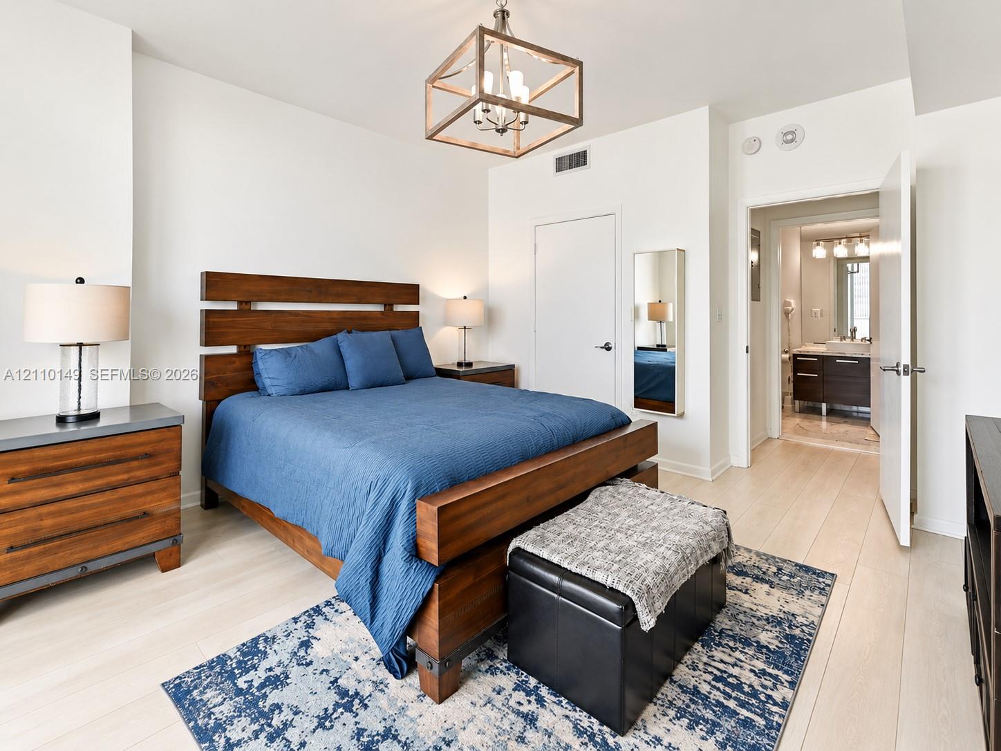 Neutral interior room featuring light wood-finish flooring, a geometric box-frame light fixture, and an integrated full-length wall mirror Neutral interior room featuring light wood-finish flooring, a geometric box-frame light fixture, and an integrated full-length wall mirror