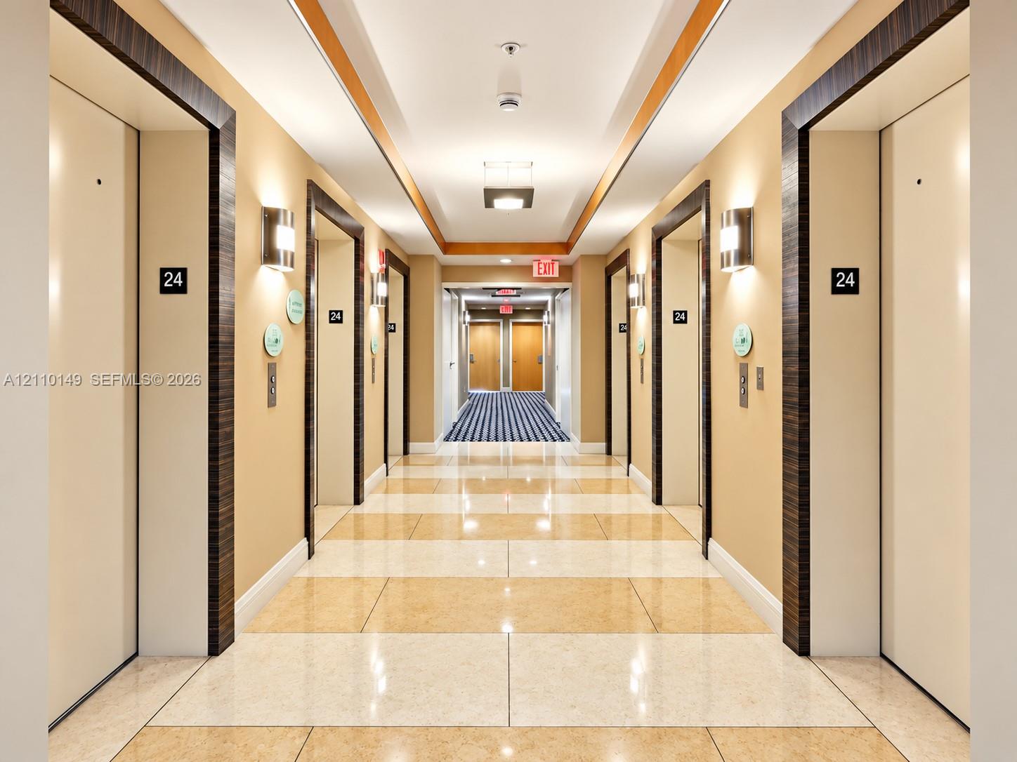 Hallway featuring high-gloss polished stone tile flooring, recessed ceiling lighting with wood-toned trim, and modern wall-mounted light fixtures