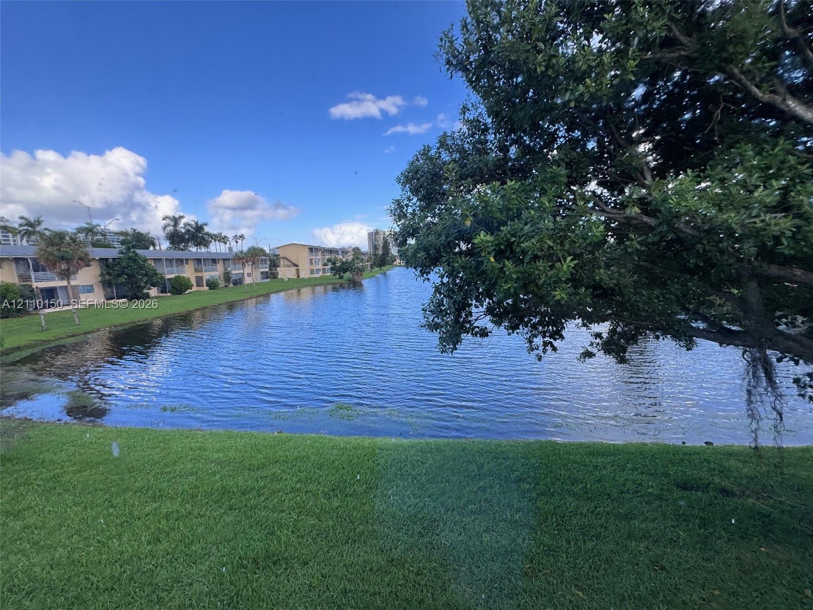 Waterfront property featuring a manicured lawn, mature trees, and a lake shoreline