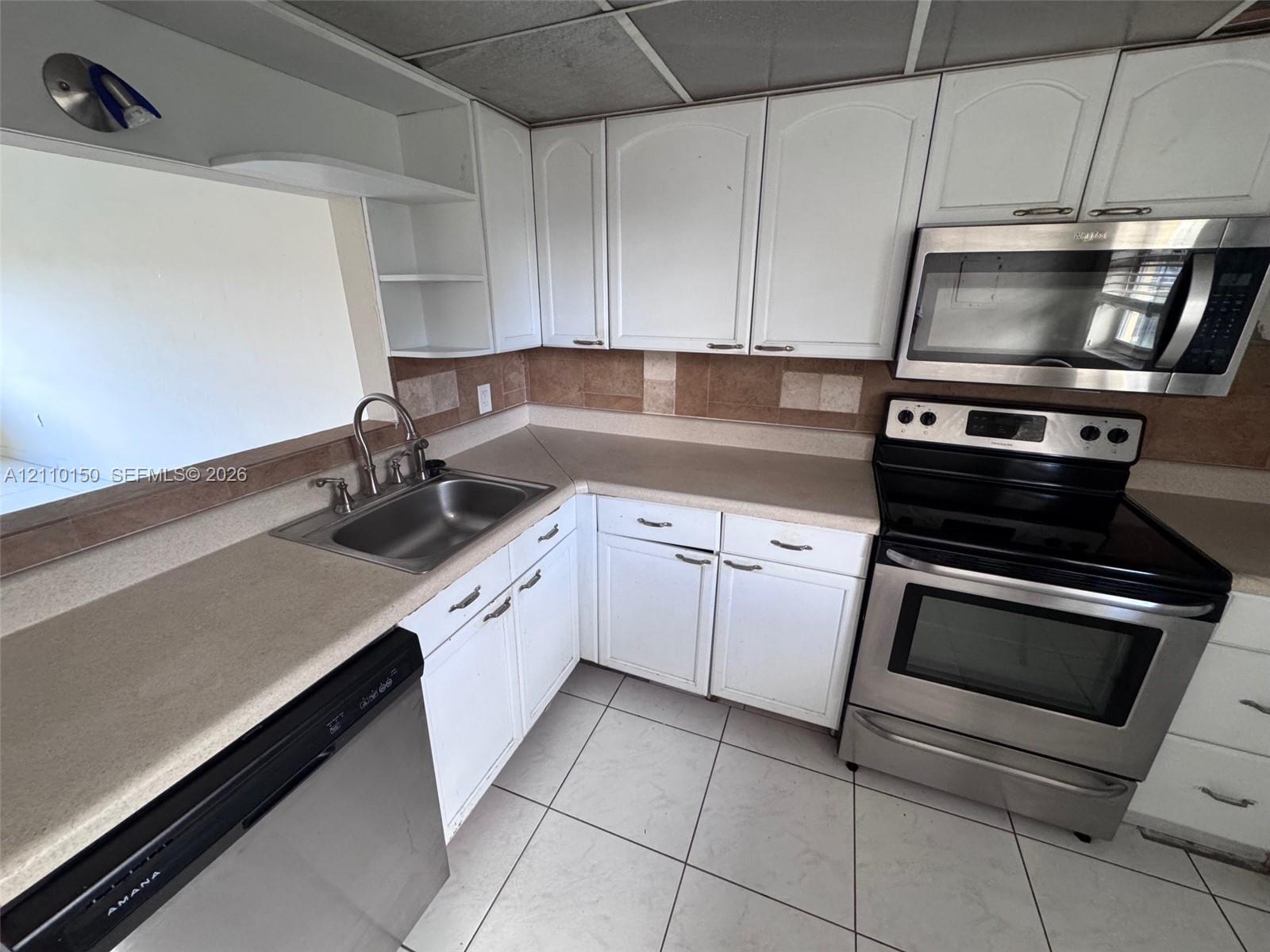 Kitchen featuring white cabinetry, stainless steel appliances, neutral countertops, tile backsplash, and tile flooring