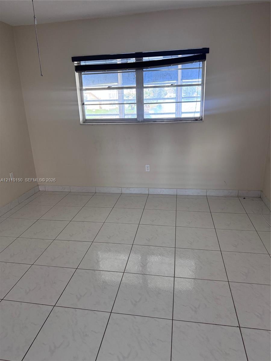Interior space featuring neutral wall paint, white tile flooring, and a multi-pane window with a horizontal window covering