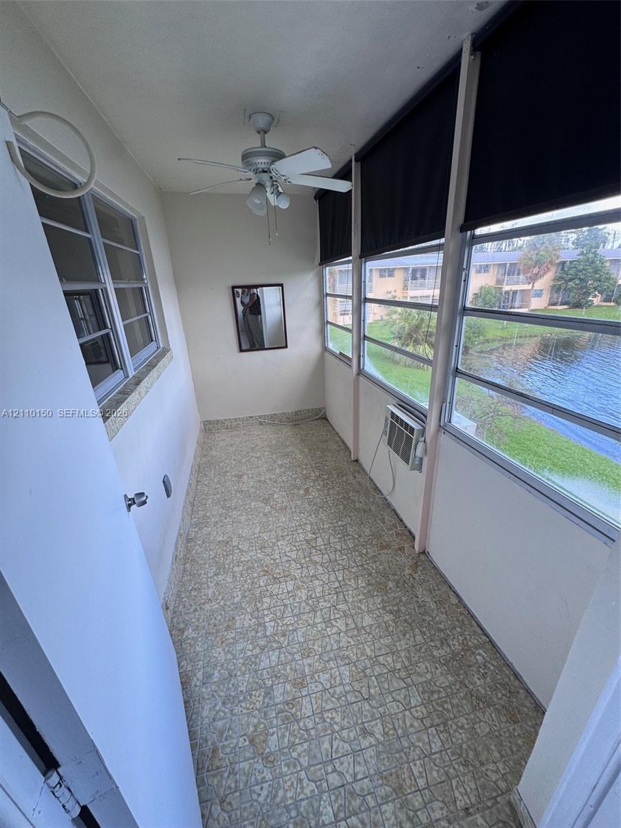 Enclosed porch featuring patterned tile flooring, a ceiling fan with integrated lighting, and multiple windows overlooking a pond