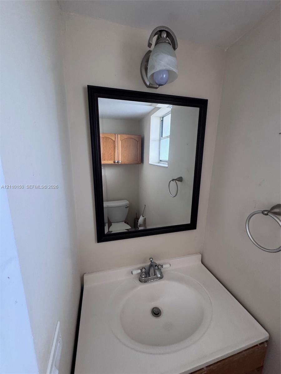 Vanity featuring an integrated white sink, dual-handle metal faucet, wall-mounted light fixture, framed mirror, and brushed-metal towel ring