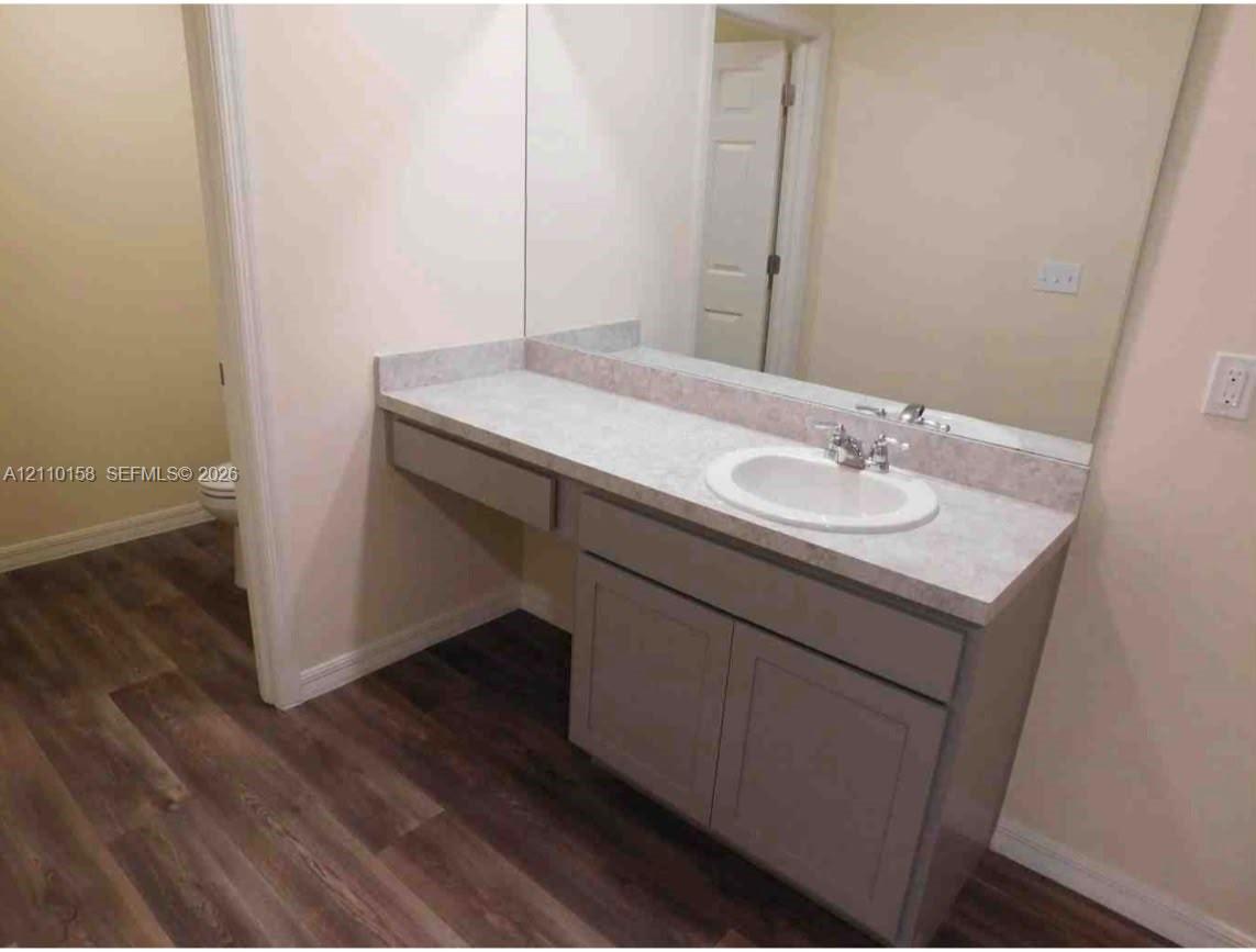 Vanity featuring a light-toned countertop, integrated basin, dual-handle faucet, grey cabinetry, and wood-finish flooring Vanity featuring a light-toned countertop, integrated basin, dual-handle faucet, grey cabinetry, and wood-finish flooring