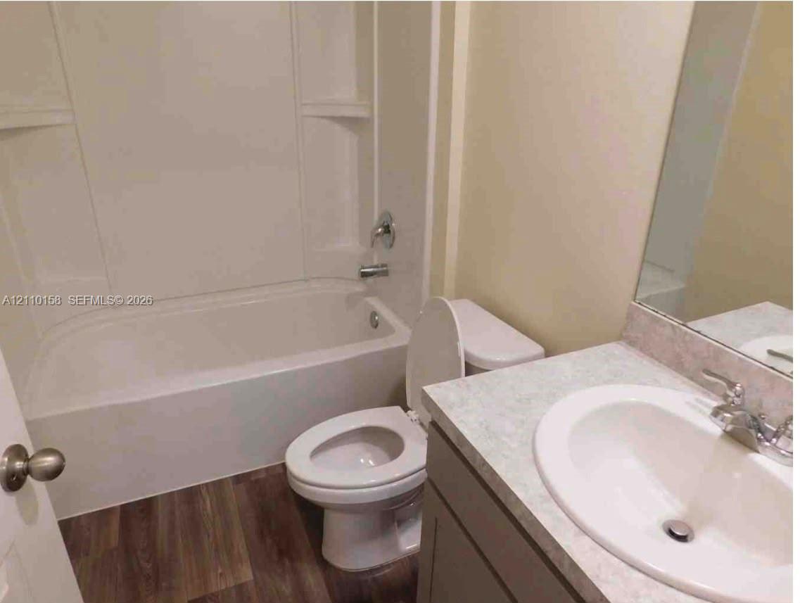Bathroom featuring a vanity with a stone-finish countertop, integrated sink, wood-finish flooring, and a tub-shower combination with a surround Bathroom featuring a vanity with a stone-finish countertop, integrated sink, wood-finish flooring, and a tub-shower combination with a surround