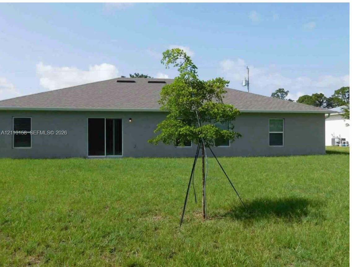 Rear exterior elevation featuring stucco siding, a hip roof with asphalt shingles, sliding glass doors, and a grass-covered backyard Rear exterior elevation featuring stucco siding, a hip roof with asphalt shingles, sliding glass doors, and a grass-covered backyard