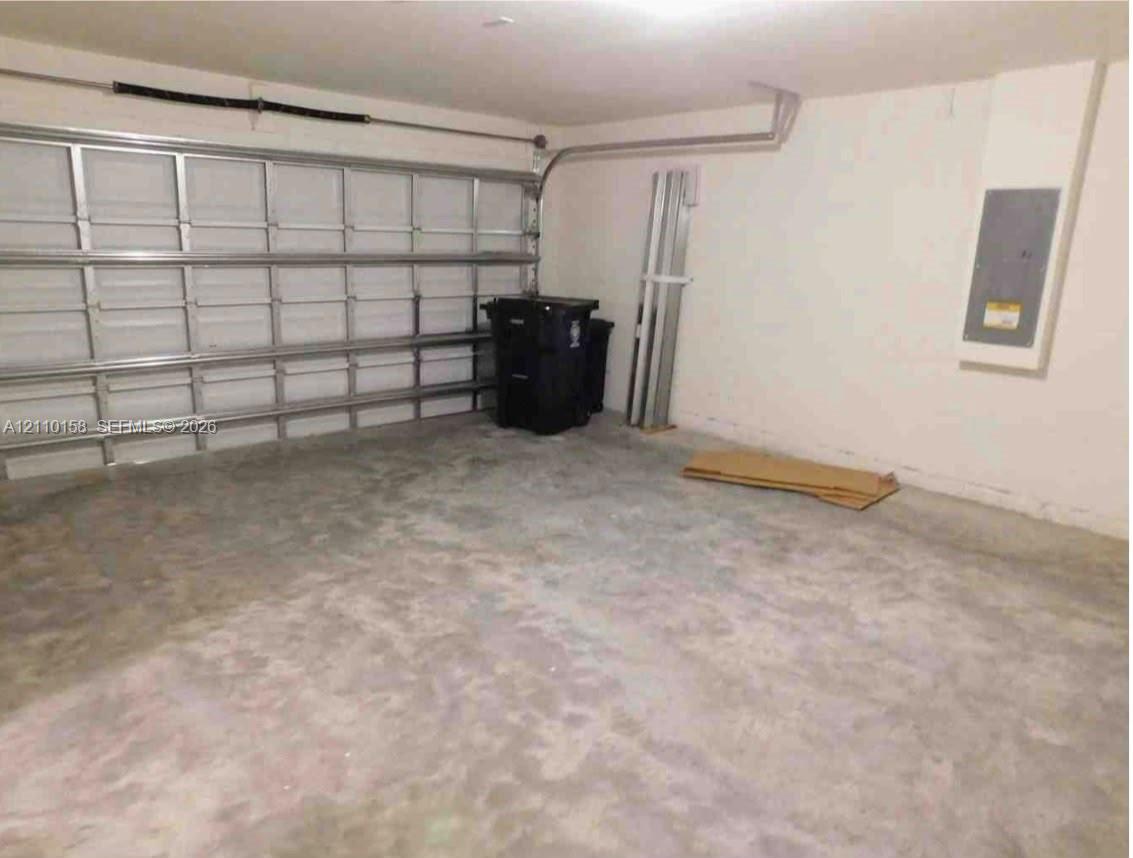 Enclosed garage space featuring a metal sectional overhead door, finished concrete flooring, and an integrated electrical service panel