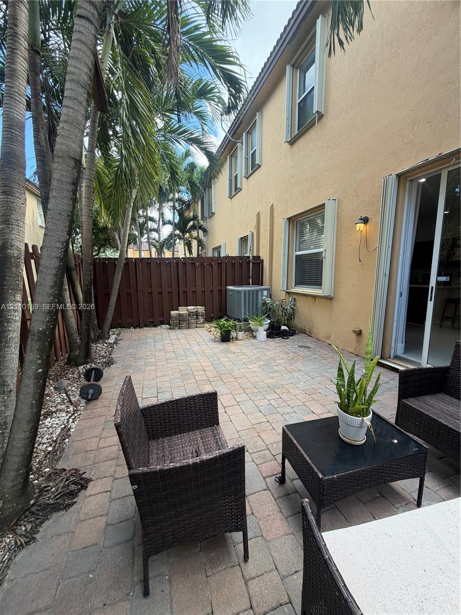Paver patio featuring a privacy fence, mature palm trees, and sliding glass door access
