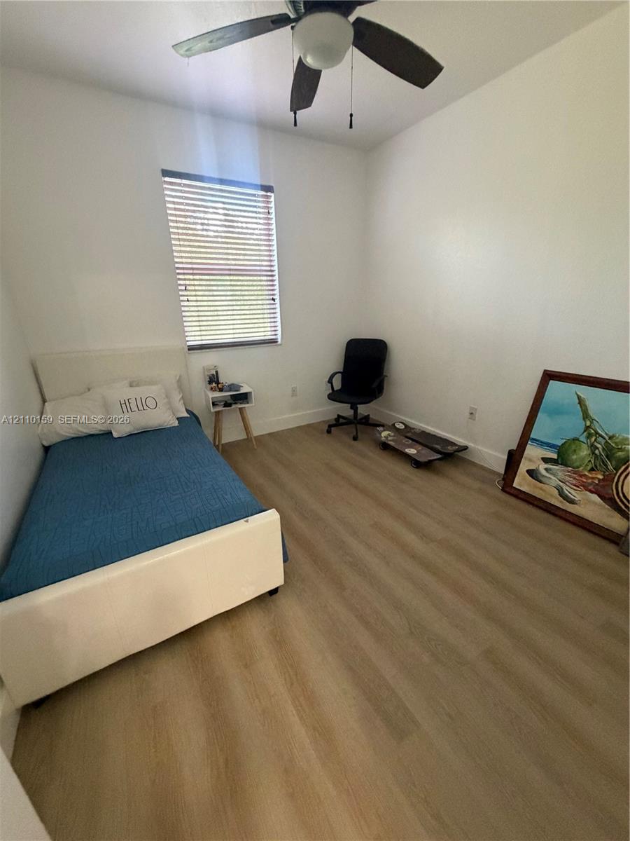 Room featuring wood-finish flooring, a neutral color palette, and a ceiling-mounted fan with integrated light fixture