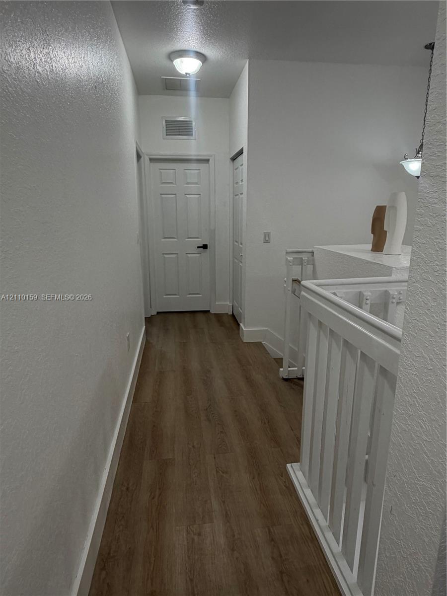 Hallway featuring wood-finish flooring, white six-panel interior doors, and a painted wooden railing