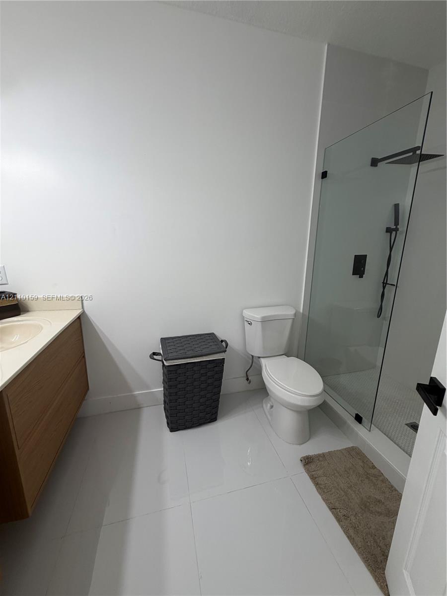 Bathroom featuring light-toned wood-finish vanity, solid surface countertop, walk-in shower with glass enclosure, and matte black shower fixtures