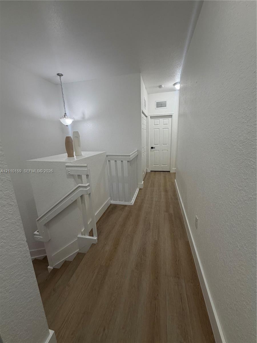 Hallway featuring wood-finish flooring, white paneled doors, and a hanging pendant light fixture with a geometric wooden balustrade