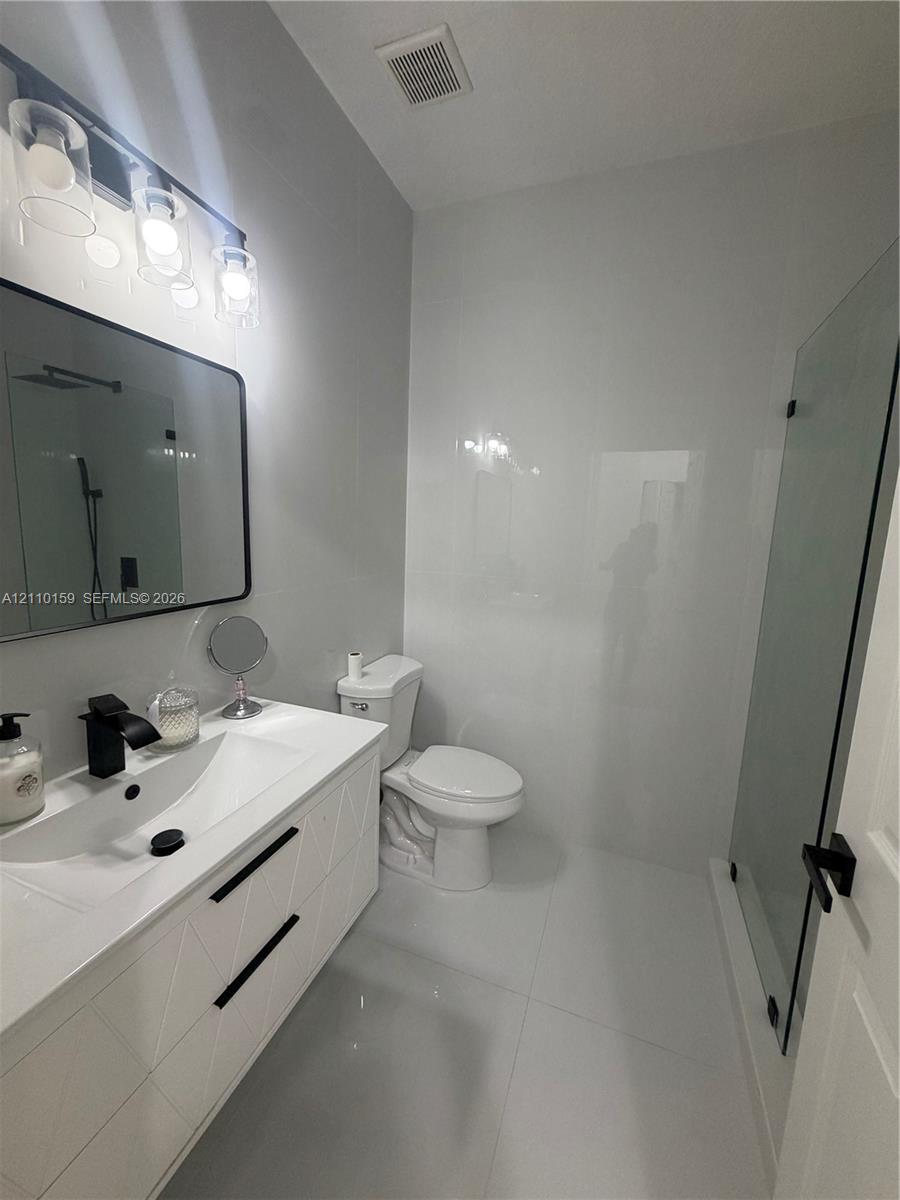Bathroom featuring a white geometric-pattern vanity, rectangular vessel sink, matte black faucet, wall-mounted rectangular mirror, and glass-enclosed shower