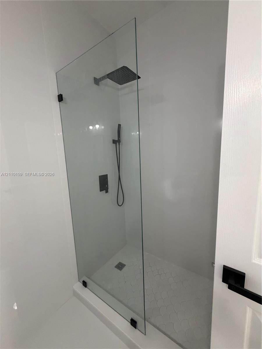 Walk-in shower featuring a frameless glass panel, matte black wall-mounted fixtures, a square rain-style showerhead, and a hand-held sprayer