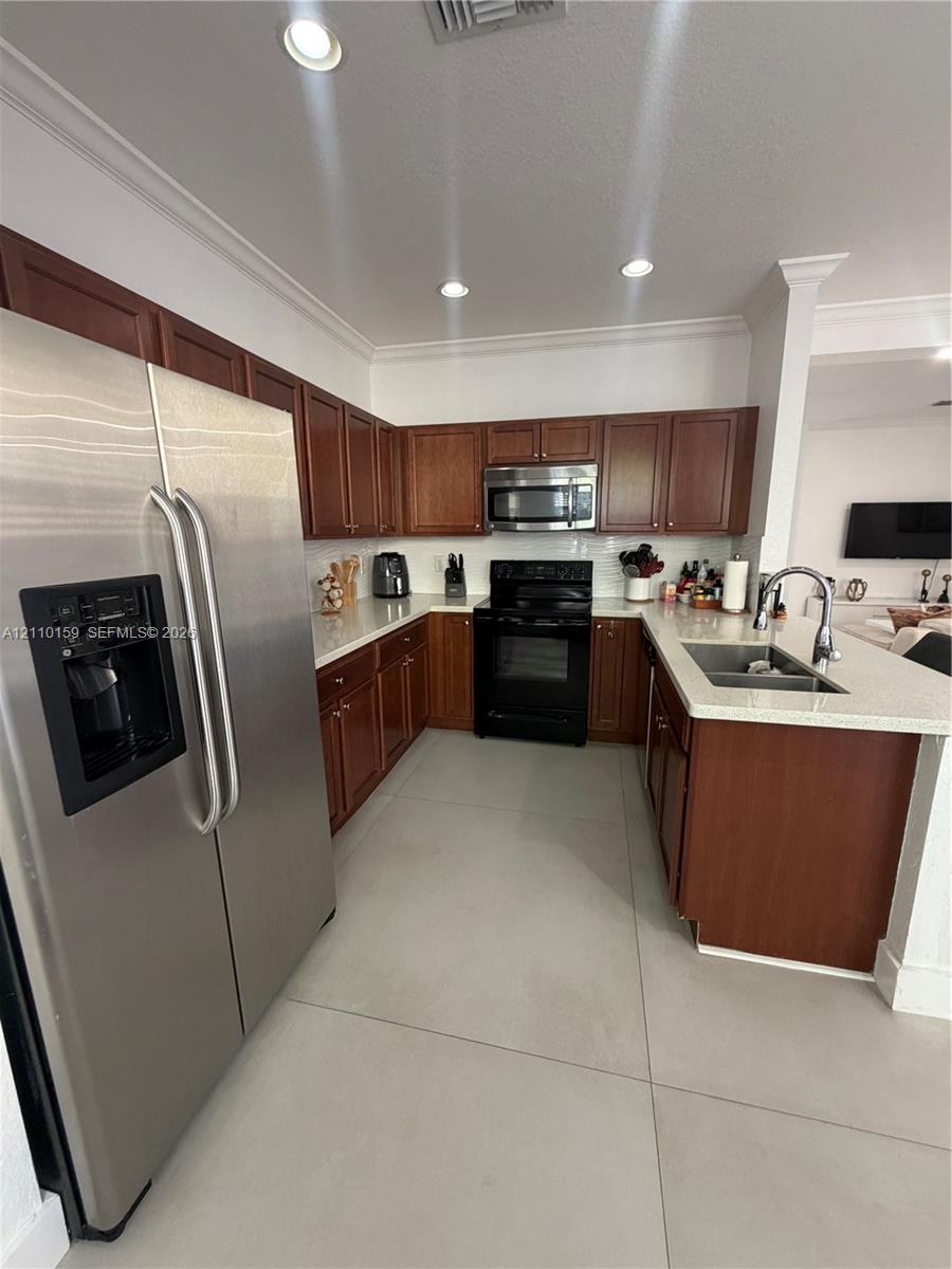 Kitchen featuring wood cabinetry, stone-finish countertops, large-format tile flooring, stainless steel side-by-side refrigerator, and built-in microwave