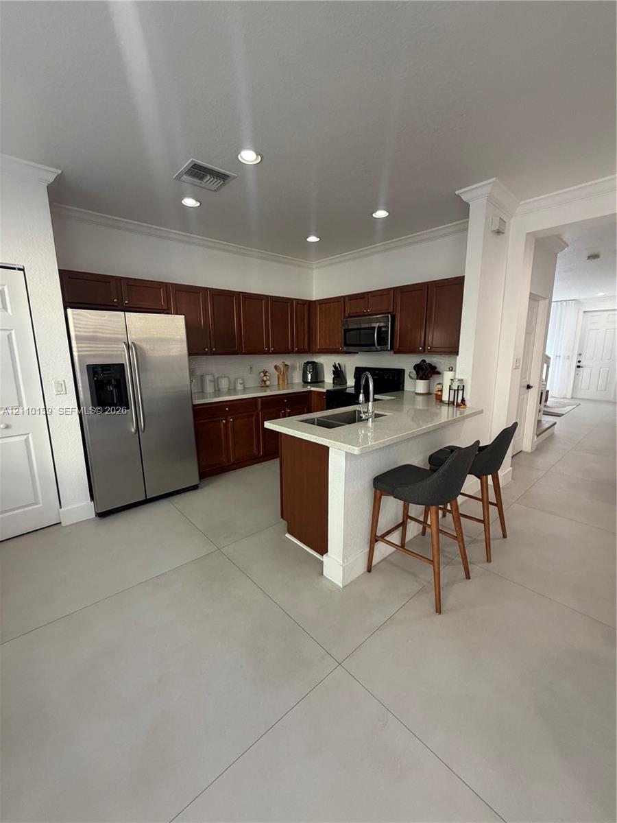 Kitchen featuring dark-toned cabinetry, light-colored countertops, stainless steel appliances, a peninsula with an undermount sink, and recessed lighting