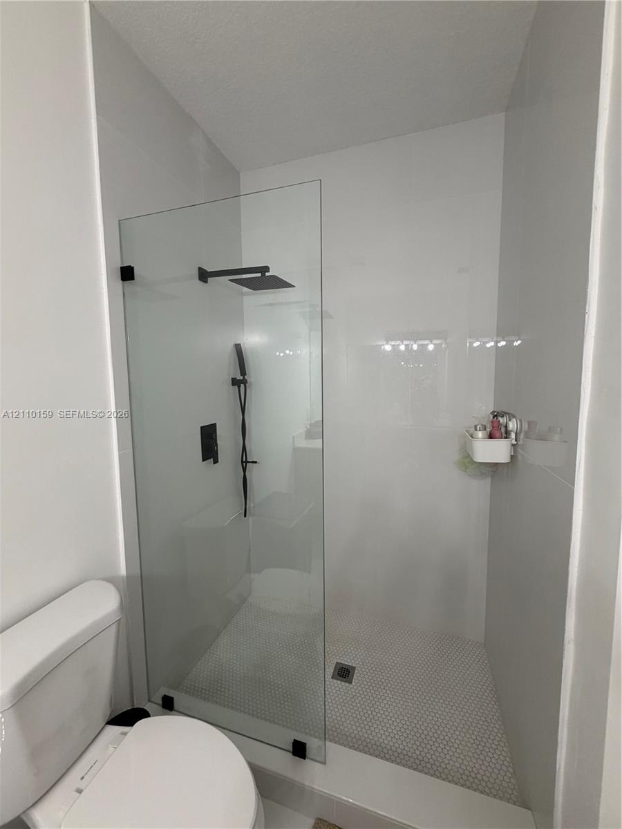 Walk-in shower featuring a frameless glass partition, matte black rainfall showerhead, handheld sprayer, and hexagon tile floor