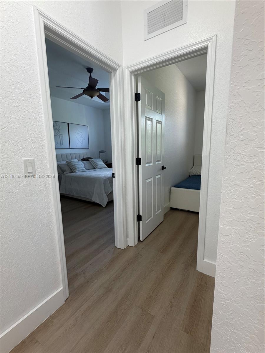 Interior hallway featuring wood-finish flooring, white door casings, and paneled doors with matte black hardware